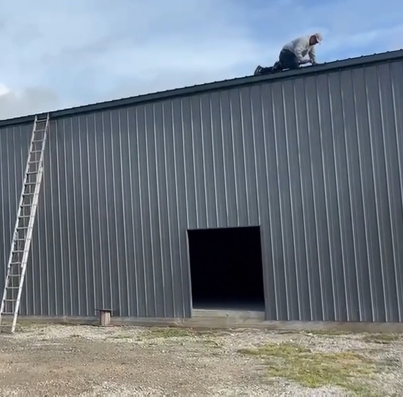Crew member working on the roof of a large metal building
